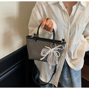 Detail of woven straw tote bag with white lace bow and faux pearl charms on black handles