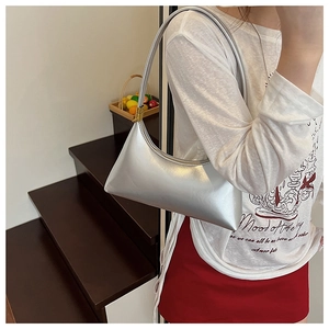 Close-up of metallic silver crescent shoulder bag worn on a model's arm for daily use