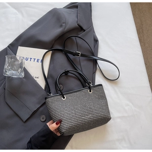 Macro detail of the woven texture and black leather handles on this stylish crossbody bag