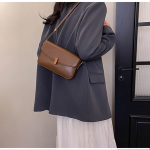 Sac à bandoulière en cuir marron avec boucle dorée porté par un mannequin en blazer gris