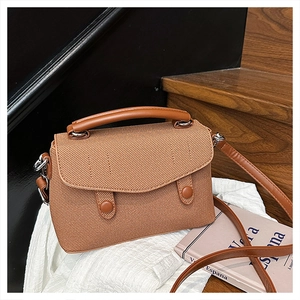Detail of caramel brown textured fabric handbag with top handle on white cloth