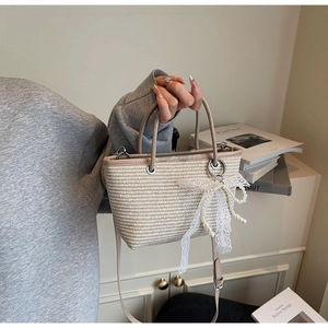 Detail of straw tote bag with white lace bow, pearl pendant and leather handles