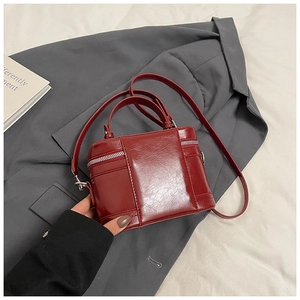 Detail einer roten glänzenden Box-Handtasche mit Schultergurt auf grauem Sakko