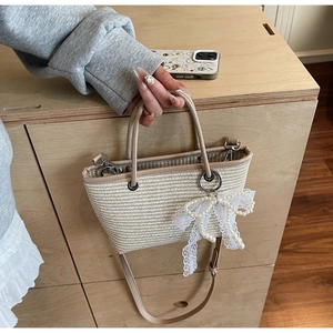 Detail view of woven straw handbag featuring pearl lace bow charm and leather handle