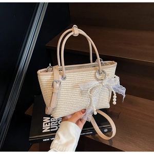 Straw handbag detail with pearl lace bow and leather strap on vintage wooden stairs
