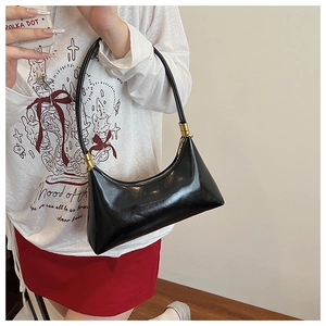 Detailed view of black crescent shoulder bag with glossy finish and gold hardware on model