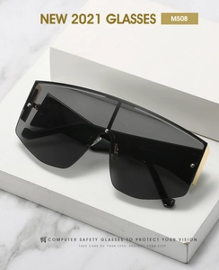 Detail of oversized shield sunglasses with dark gray lenses and golden metal hinges
