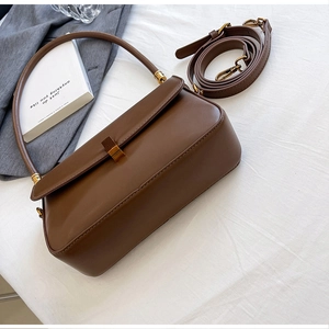 Sac bandoulière en cuir marron vintage avec boucle dorée posé sur un blazer gris