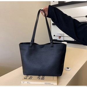 Close-up of black leather tote bag with fine litchi texture and slim shoulder straps