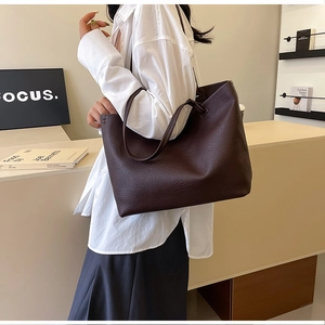 Detail of large brown tote bag showing pebbled leather texture and thin shoulder straps