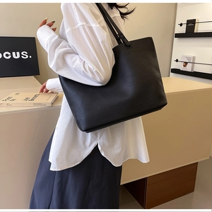 Side view of large black tote bag with lychee texture leather worn by model