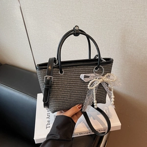 Elegant black and white woven straw tote bag with pearl bow charm and leather handles
