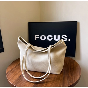 Cream lychee leather tote bag with thin straps on a dark wooden table in home setting