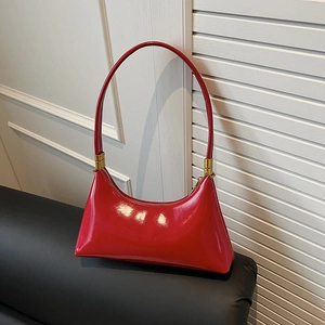 Glossy red patent leather crescent shoulder bag with gold hardware against window blinds