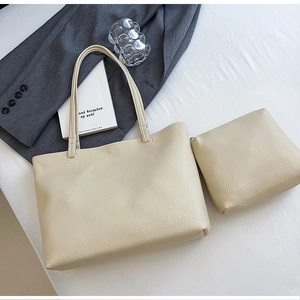 Detail of creamy white pebble grain leather tote bag with matching inner pouch on a bed