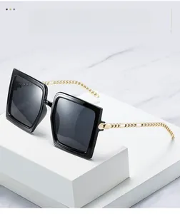 Detail of oversized square sunglasses with gold chain-link metal temples on marble