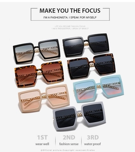 Flat lay of square sunglasses with gold chain temples in multiple color variations