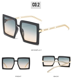 Detail view of large square sunglasses featuring gold metal chain temples and gradient lenses