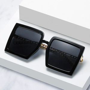 Oversized black square sunglasses with decorative gold chain on geometric background