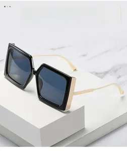 Lunettes de soleil carrées noires avec branches en métal doré sur fond de marbre blanc