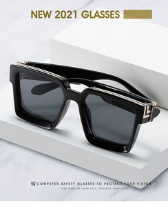 Close-up of black oversized square sunglasses with gold metal hinges on display stand