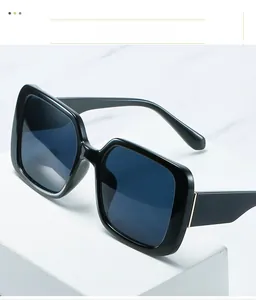 Close-up of square black sunglasses with gold metal temple details on white marble