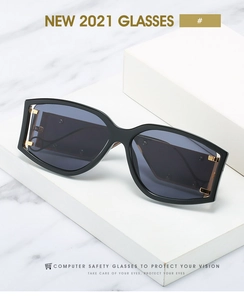 Détail de lunettes de soleil oversize noires avec boucles dorées sur socle blanc