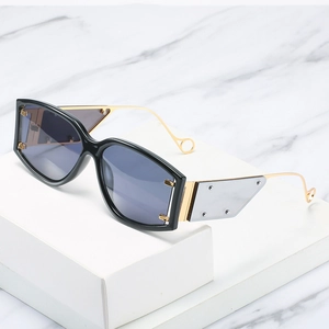 Lunettes de soleil oversize noires avec branches dorées sur présentoir en marbre