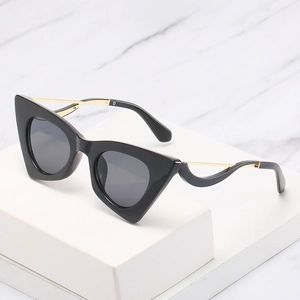 Lunettes de soleil œil-de-chat rétro avec monture noire et branches dorées sur marbre