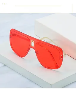 Détail de lunettes de soleil sans monture rouges avec clous dorés et cadre en métal