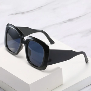 Lunettes de soleil carrées noires surdimensionnées avec branches larges sur marbre