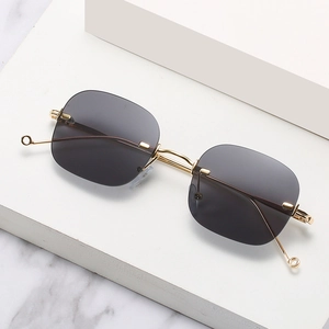 Retro rimless sunglasses with gold metal temples and dark gray square lenses on marble stand