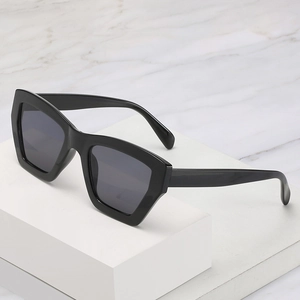 Modern black geometric square sunglasses with dark grey lenses on a white marble pedestal