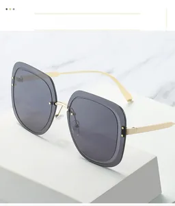 Close-up of square sunglasses with grey lenses and slim gold metal temples on a stone base