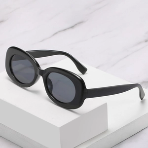 Chic oval sunglasses with black frame and grey lenses on a white geometric stand