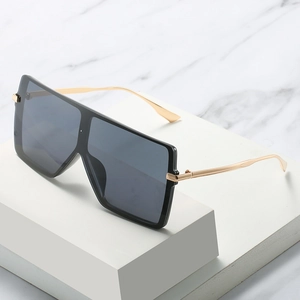 Oversized square shield sunglasses with black lenses and gold metal temples on marble
