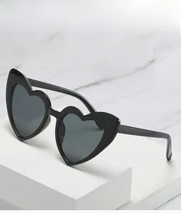 Close-up of trendy heart-shaped sunglasses with black thick frames on a marble base