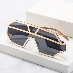 Occhiali da sole geometrici oversize in metallo dorato con lenti grigie su piedistallo bianco
