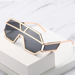 Occhiali da sole futuristici con montatura geometrica dorata e grandi lenti grigie su marmo