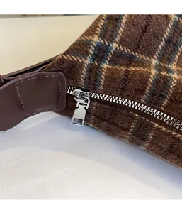 Detail of brown plaid tweed fabric with silver metal zipper and leather strap attachment
