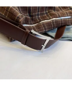 Detail of adjustable dark brown leather strap with silver square buckle on plaid shoulder bag