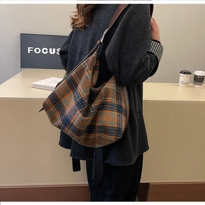 Detail of a vintage plaid tote bag featuring brown and orange tweed texture with leather strap