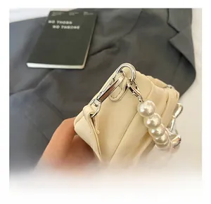 Detailed close-up of cream pleated handbag featuring pearl handle and silver metal hardware