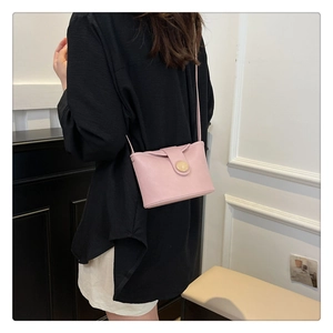 Detail of soft leather shoulder bag in light pink with circular clasp on a female model