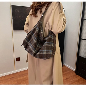Detail of a large checkered hobo bag with leather strap worn over a khaki trench coat