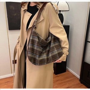 Detail of large capacity plaid tote bag with brown leather strap on model in trench coat