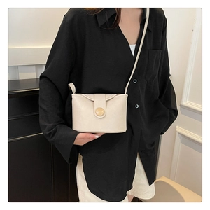 Beige soft leather crossbody bag with round button flap worn by model in minimalist setting