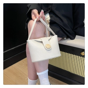 Detail of soft cream faux leather handbag with circular decorative buckle and top handle