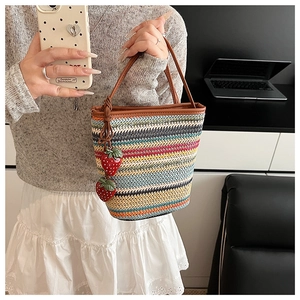 Détail du sac à bandoulière tissé à rayures colorées avec breloques fraises et bandoulière cuir