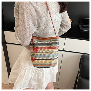 Détail du sac seau tissé coloré avec des breloques fraises et une bandoulière en cuir